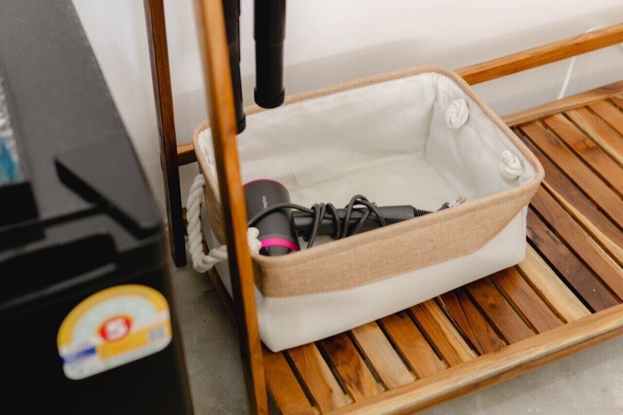 A small, open storage basket with a white interior and a beige exterior, placed on a wooden slatted shelf.