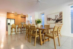 A modern kitchen with wooden cabinets, a dining area with a table and chairs, and a ceiling fan.