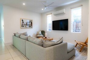 Ein Wohnzimmer mit einem Ecksofa, einem flachbildfernseher an der Wand, einem Deckenventilator und einem Fenster mit Blick.