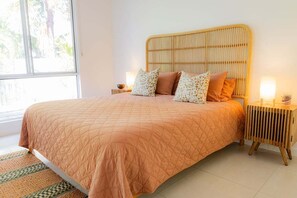 A bedroom with a large bed, a wooden headboard, two bedside tables with lamps, and a view of the outdoors through a window.