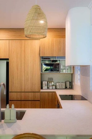 A modern kitchen with wooden cabinets, a built-in microwave, and a hanging light fixture.
