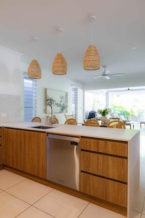 A modern kitchen with wooden cabinets, a built-in dishwasher, and pendant lights. - Waves | 3 Bedroom Holiday Home (Palm Cove)