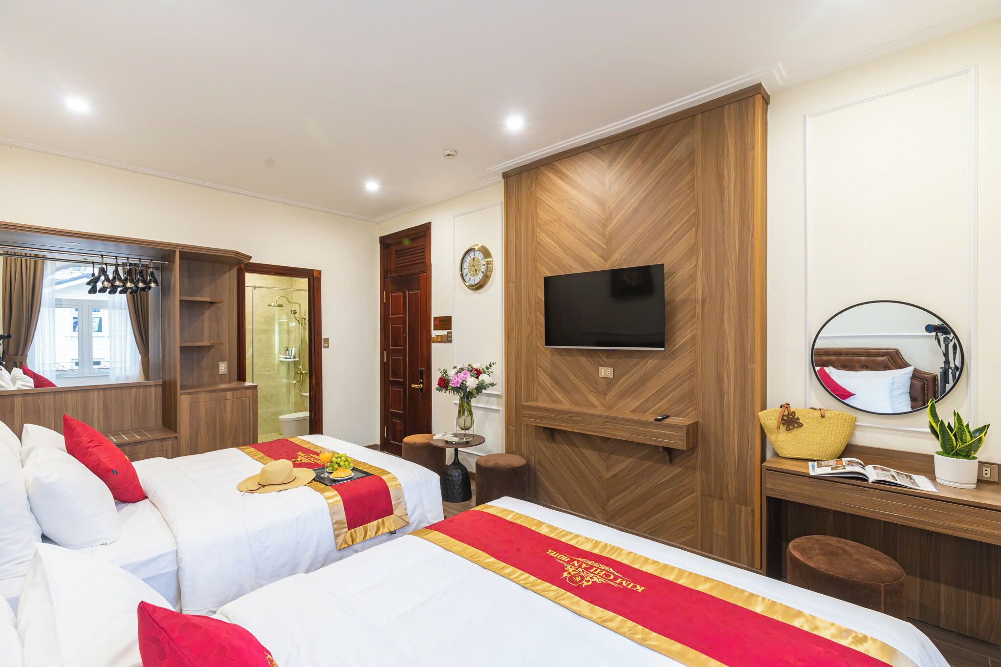 A hotel room with two beds, a TV, a desk, and a mirror.