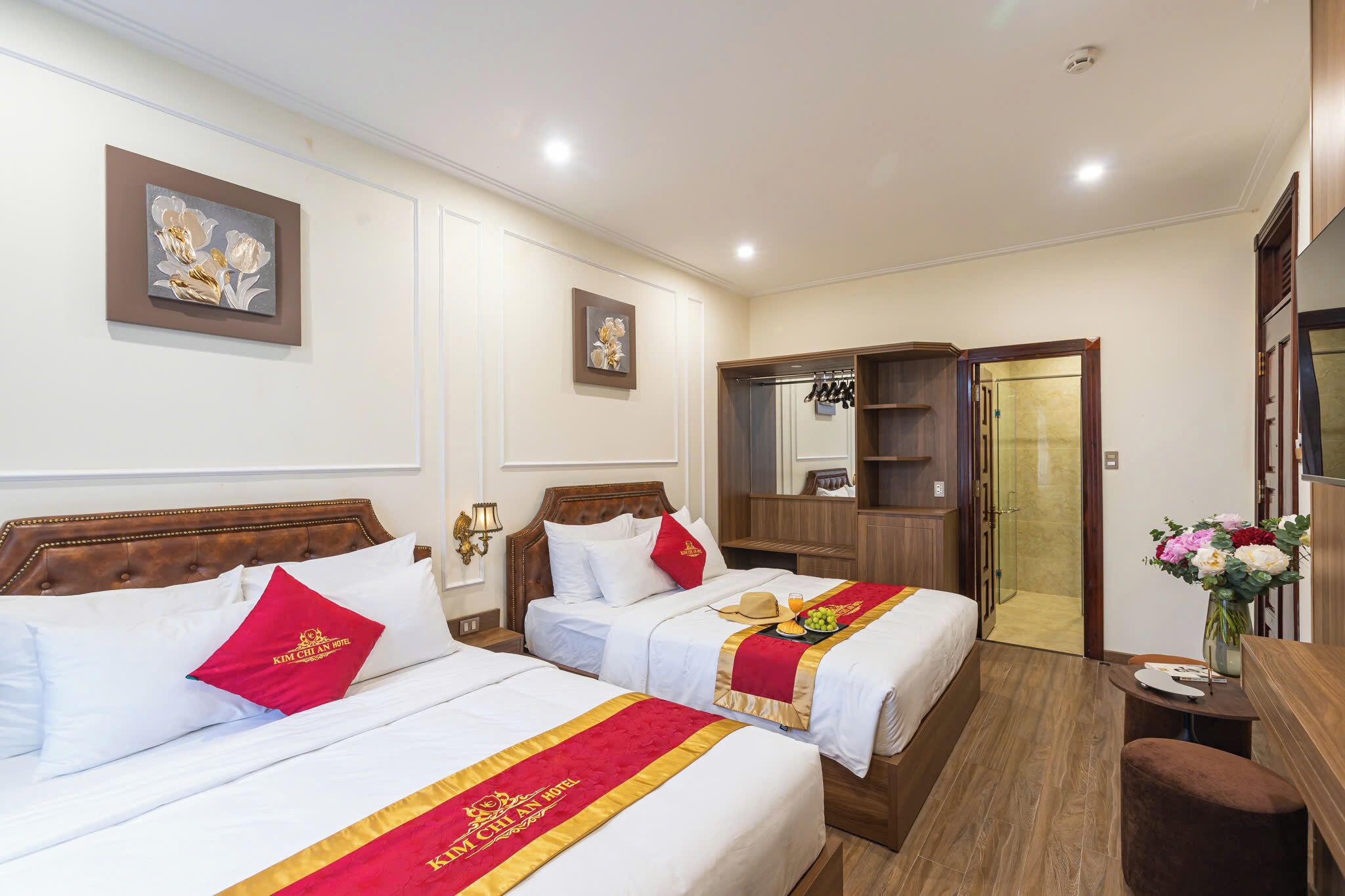 A hotel room with two beds, a wooden wardrobe, a desk, and a shower area.