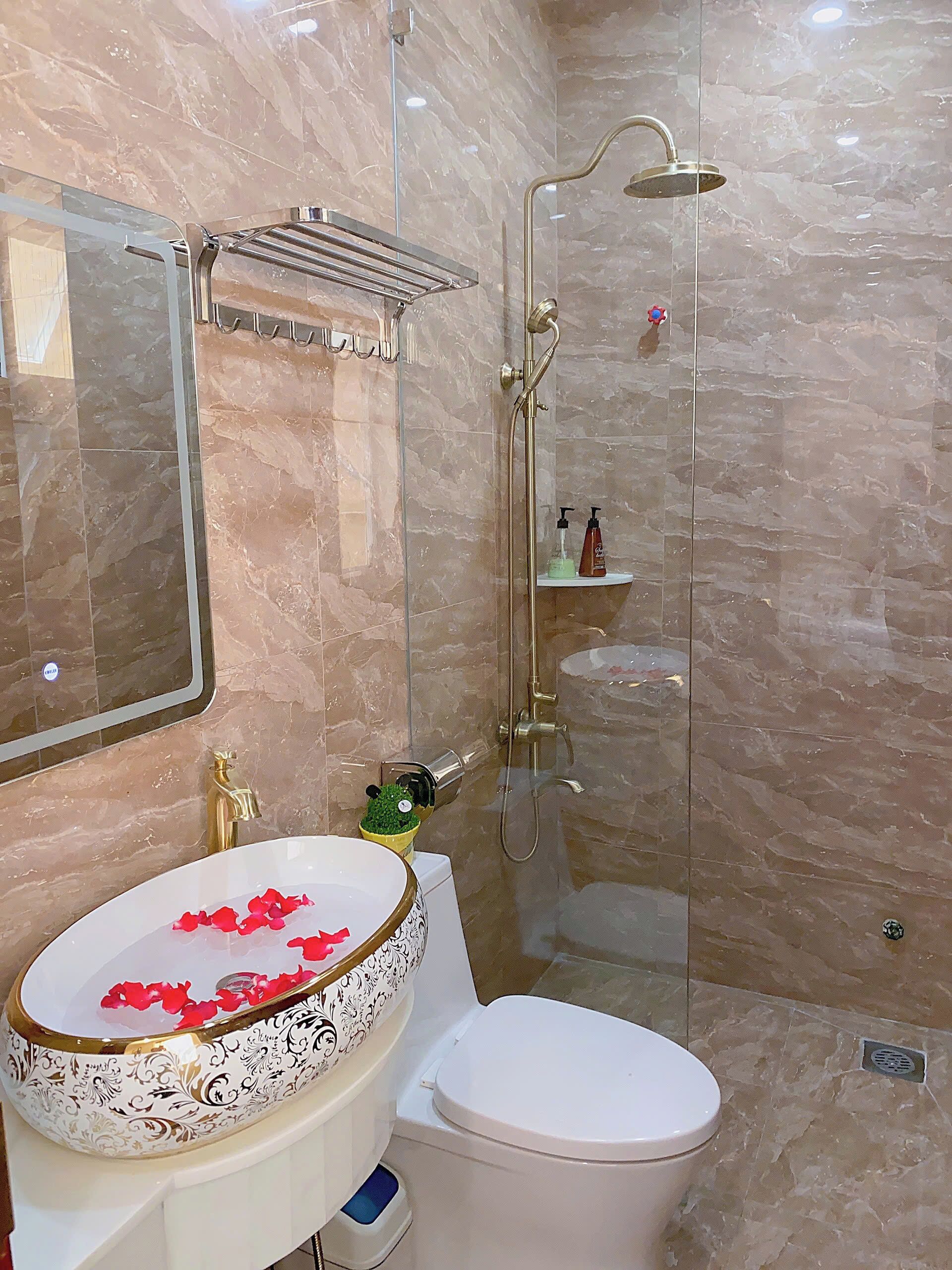 A bathroom with a marble floor, a white toilet, a glass-enclosed shower, and a sink with a decorative bowl.