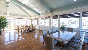 Un comedor amplio con una mesa grande y sillas, ventanas amplias con persianas y un techo alto con tragaluces.