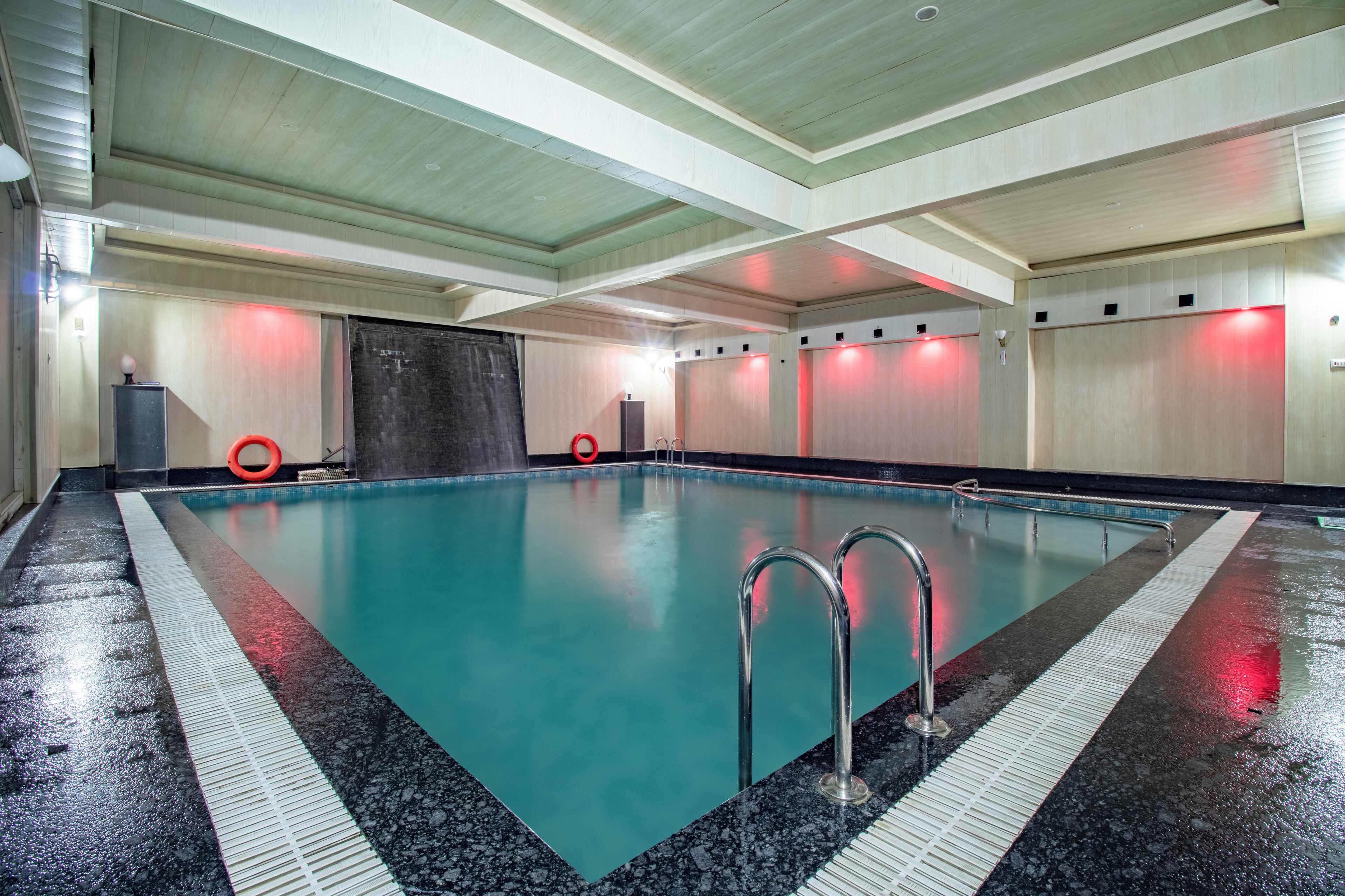 An indoor swimming pool with clear water, metal ladders, and red lighting accents.