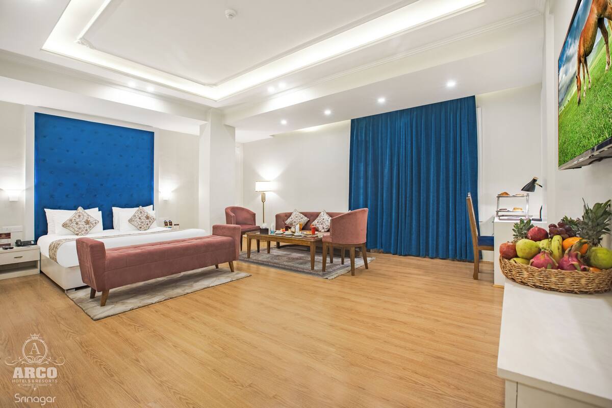 A hotel room with a bed, a sofa, a coffee table, and a fruit basket.