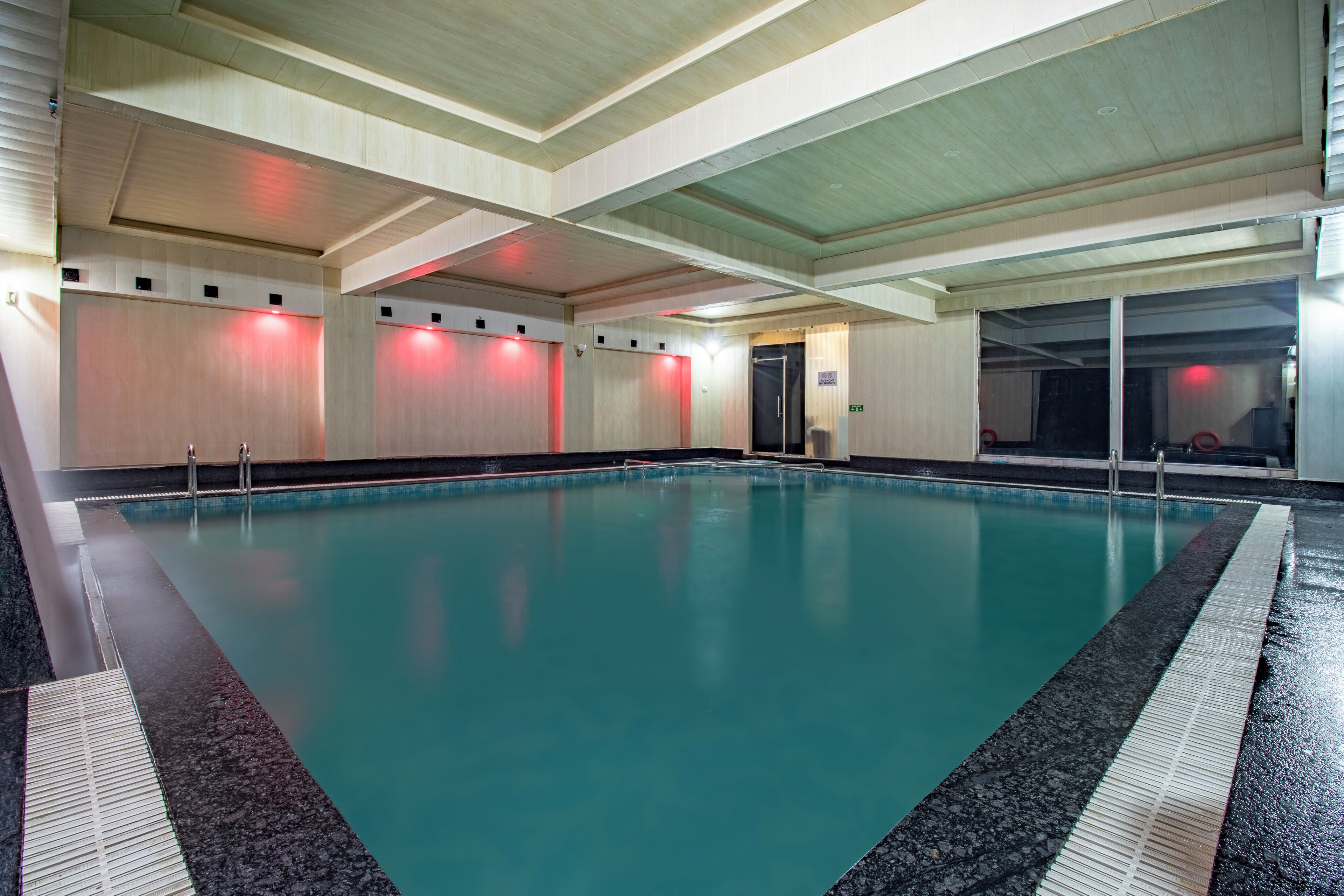 An indoor swimming pool with a tiled floor, a wooden ceiling, and red lighting.