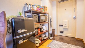 Une cuisine compacte avec un réfrigérateur noir, un four à micro-ondes et une étagère contenant divers objets, notamment des boîtes de céréales.