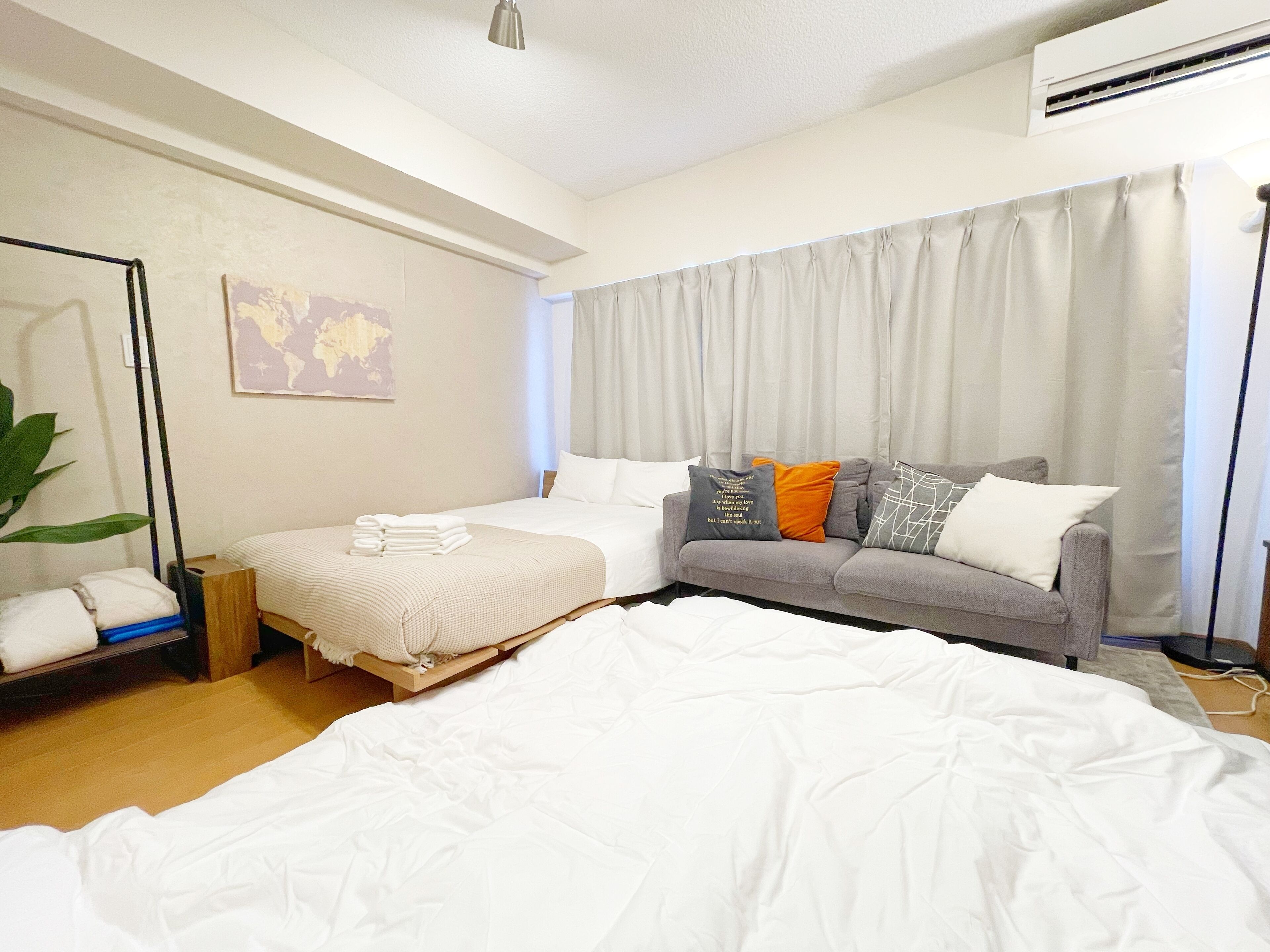 A hotel room with a bed, a sofa, a world map on the wall, and a large window with curtains.