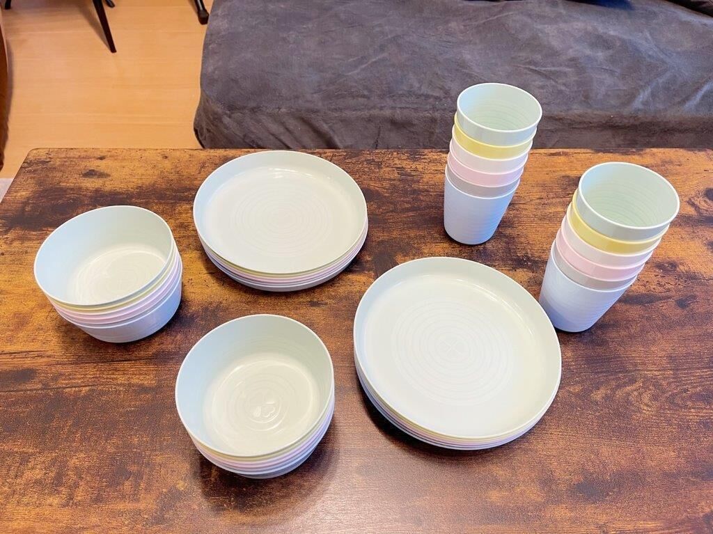 Et træbord med stakke af hvide tallerkener og farverige plastikkopper.