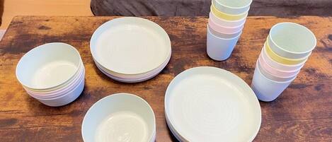 Et træbord med stakke af hvide tallerkener og farverige plastikkopper.