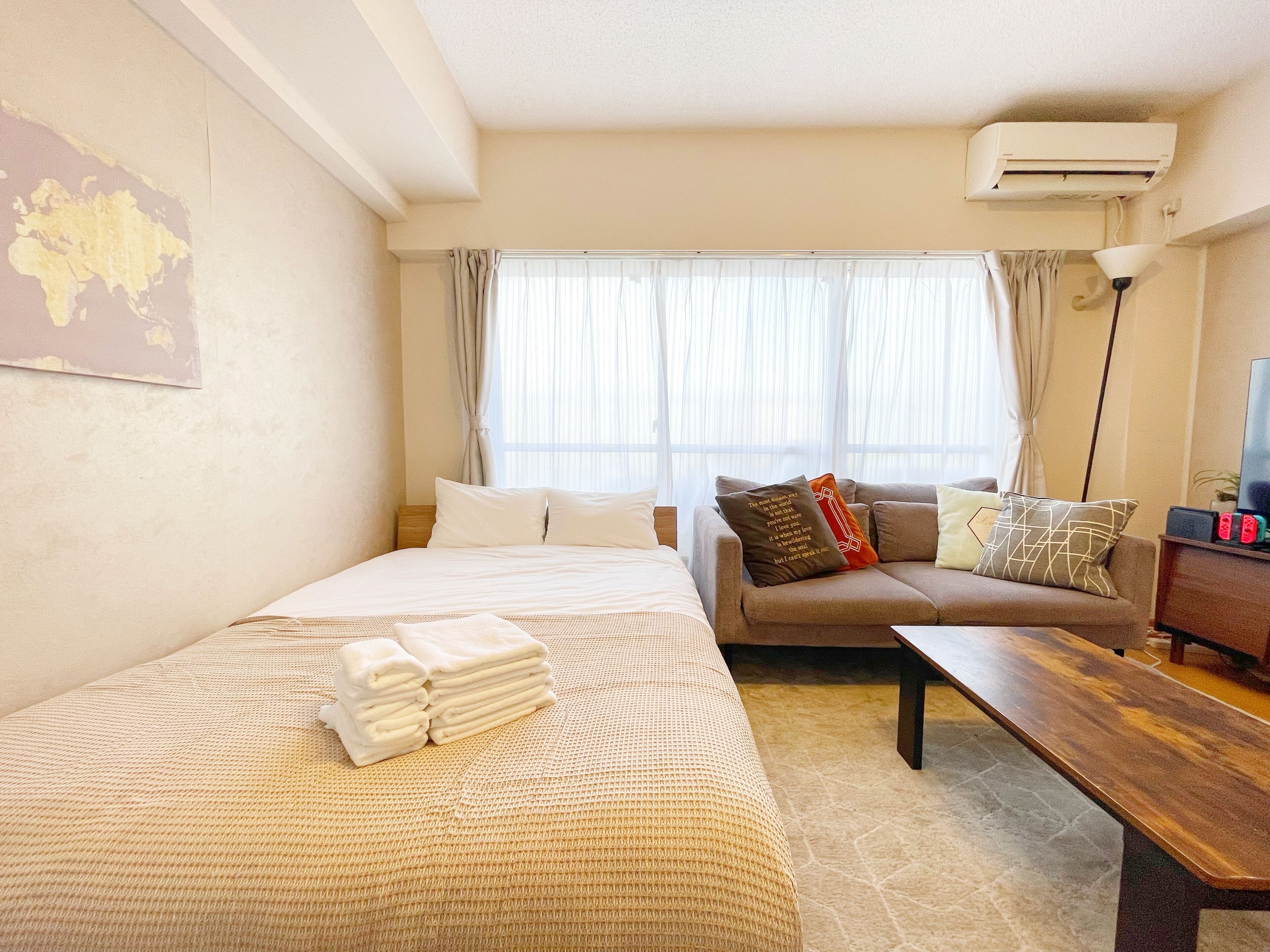 Habitación de hotel con cama, sofá, escritorio y un amplio ventanal con cortinas.