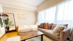 Un salon moderne avec un canapé, une table basse en bois, un lit avec une couette blanche, une plante suspendue et une carte du monde accrochée au mur.