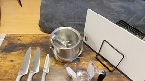 Une table en bois, un récipient en acier inoxydable, un verre à mesurer et deux couteaux.