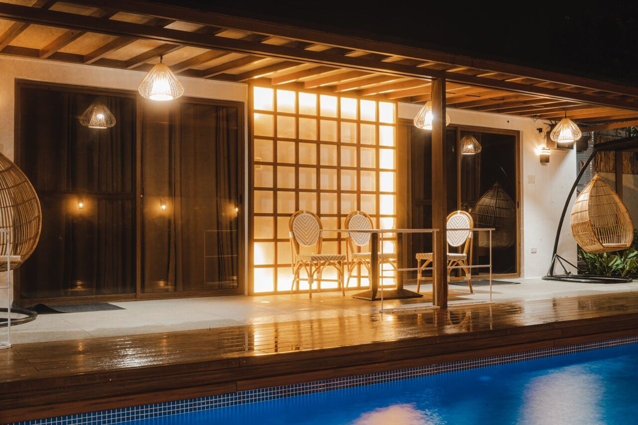 A poolside area with a wooden pergola, wicker chairs, and a tiled pool.