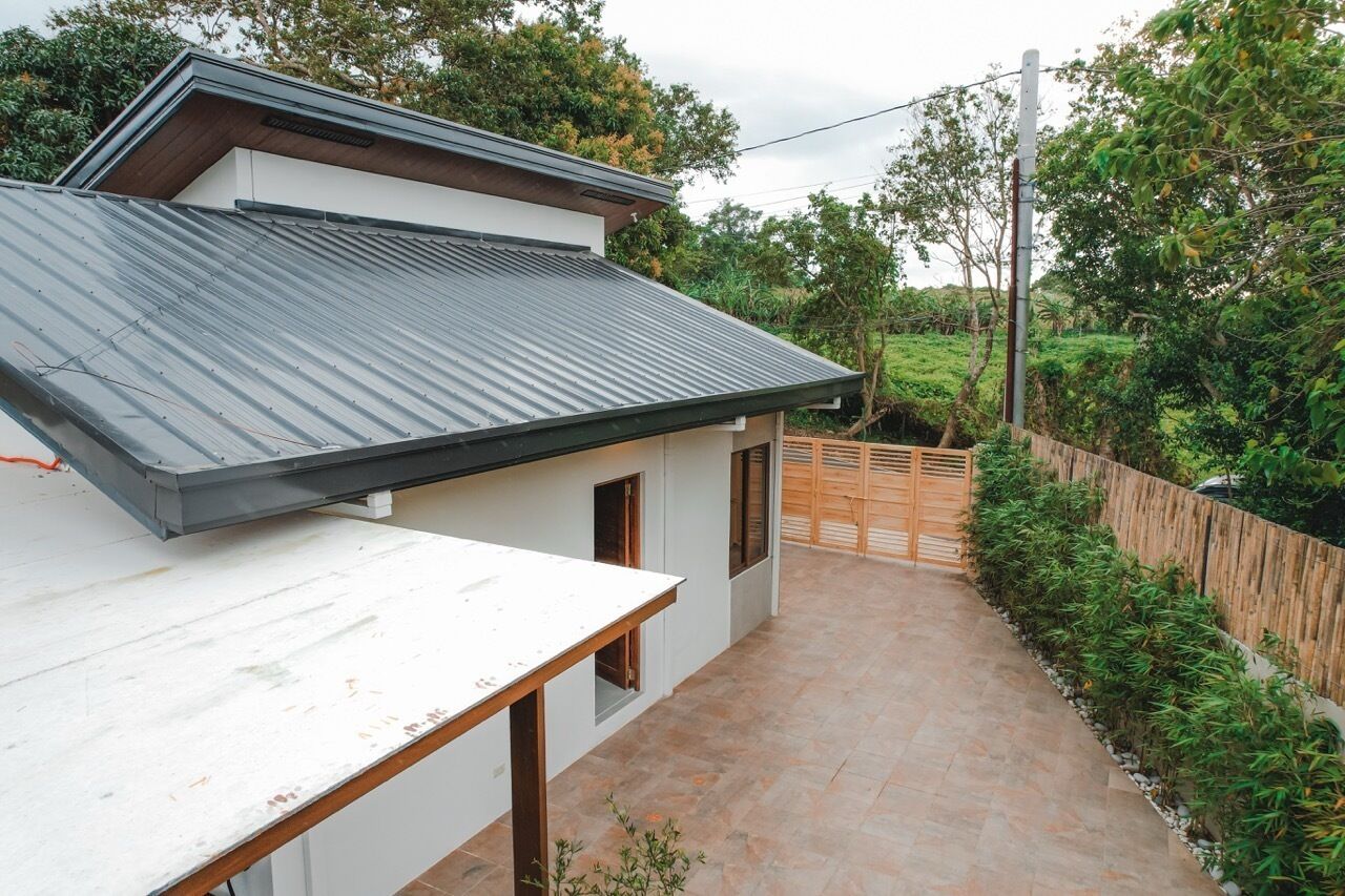 Una casa moderna con techo metálico inclinado, un porche pequeño y un patio pavimentado.
