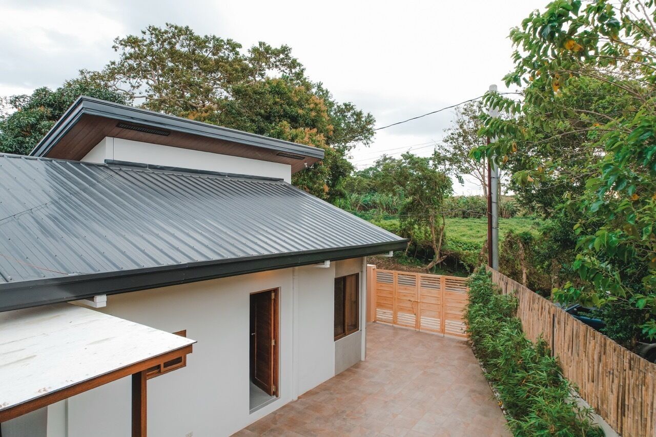 A modern house with a sloped metal roof, a small attached garage, and a paved pathway leading to a wooden gate.