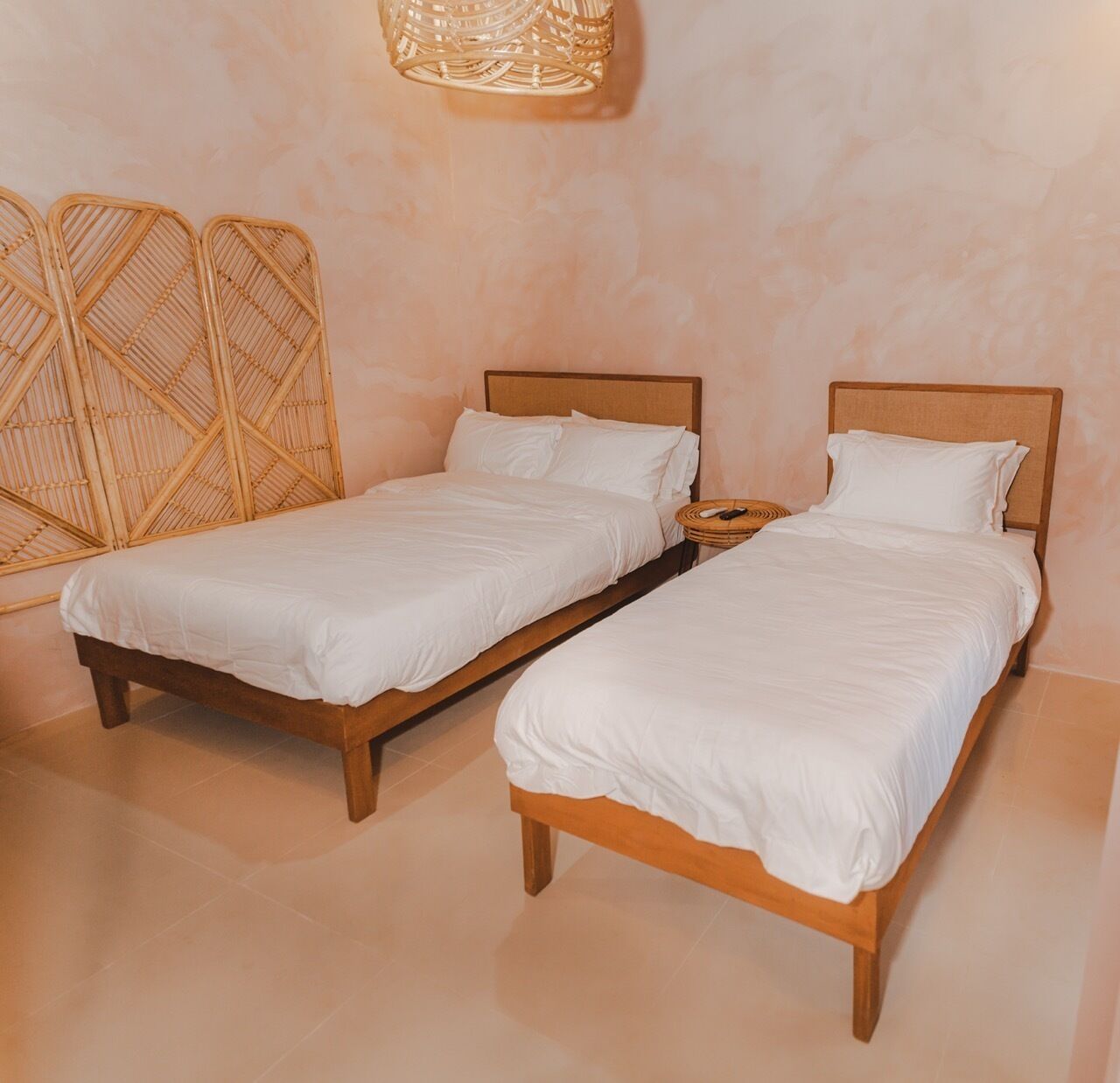 Two wooden beds with white bedding in a room with a textured wall and a woven light fixture.