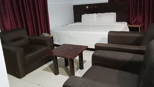 Una habitación de hotel con una cama, dos sillones, una mesita y una mesita de noche.