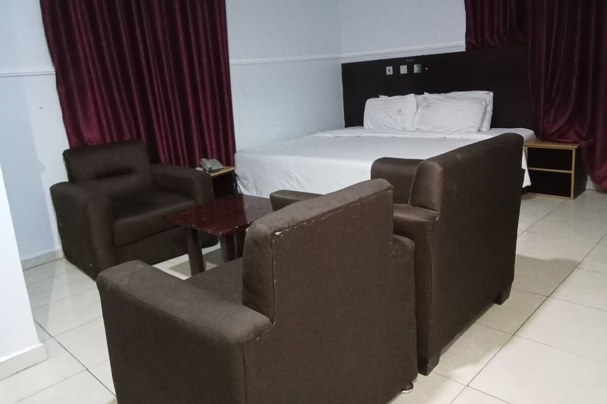 A hotel room with a bed, two armchairs, a small table, and a nightstand.