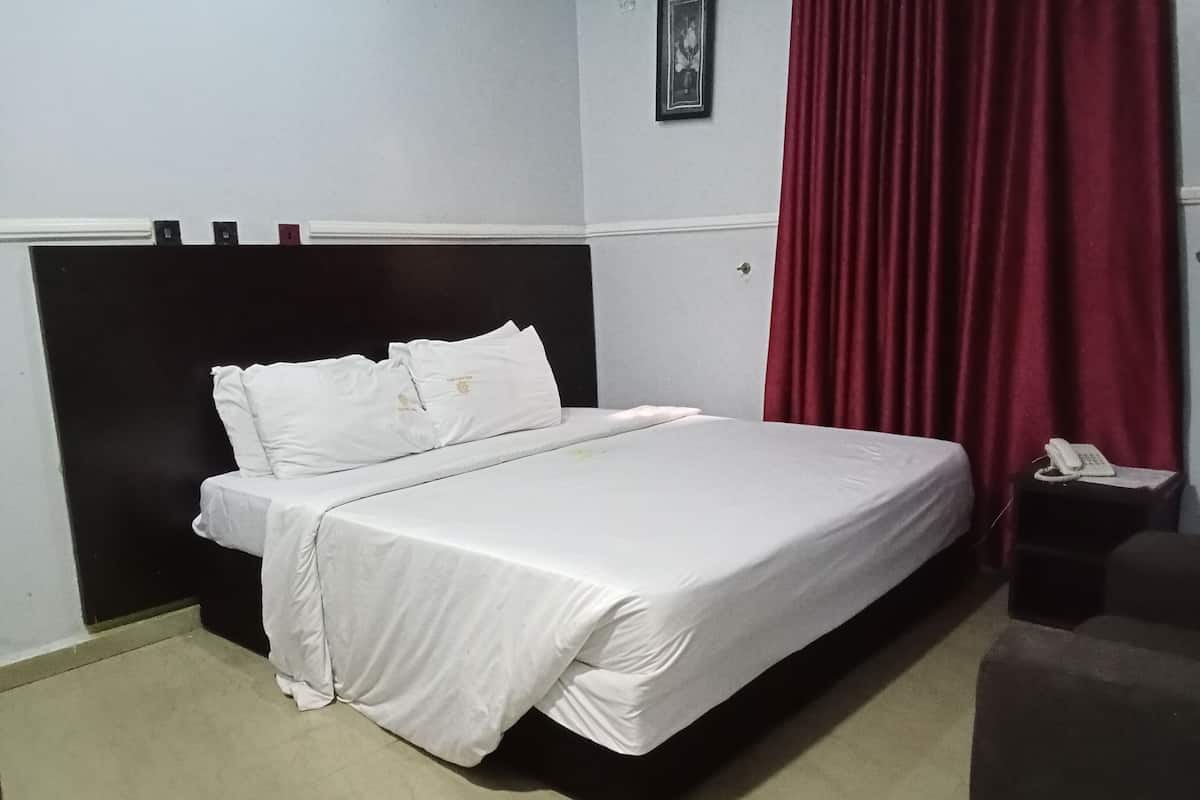 A neatly made bed with white bedding in a room with a black headboard, a red curtain, and a small bedside table with a phone.
