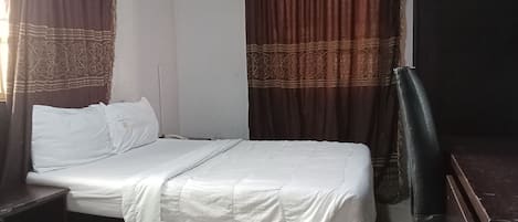 Una cama individual con cubrecama blanco, una mesita de noche, una silla y un armario.