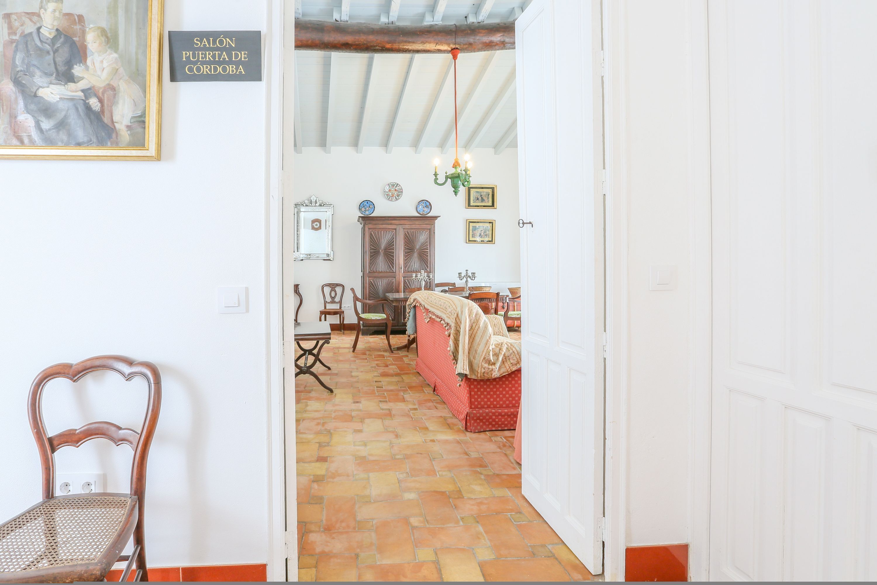 A hallway leading to a room with a red bed, a wooden cabinet, and a chair.