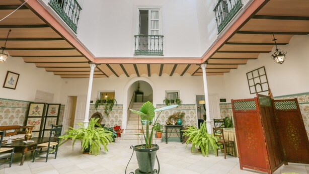 A spacious courtyard with a dining area, potted plants, and a staircase leading to an upper level. - Posada De La Casa Del Pintor Hab Malaga (Carmona)