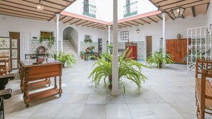 A spacious indoor area with a high ceiling, a staircase leading to an upper level, and multiple potted plants. - Posada De La Casa Del Pintor Hab Malaga (Carmona)