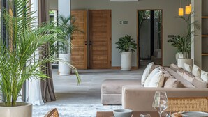 A spacious living area with a wooden dining table, comfortable seating, and large potted plants. - Villa Amanora (Canggu)