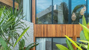 A modern building entrance with a stone pathway leading to glass doors, surrounded by large potted plants. - Villa Amanora (Canggu)