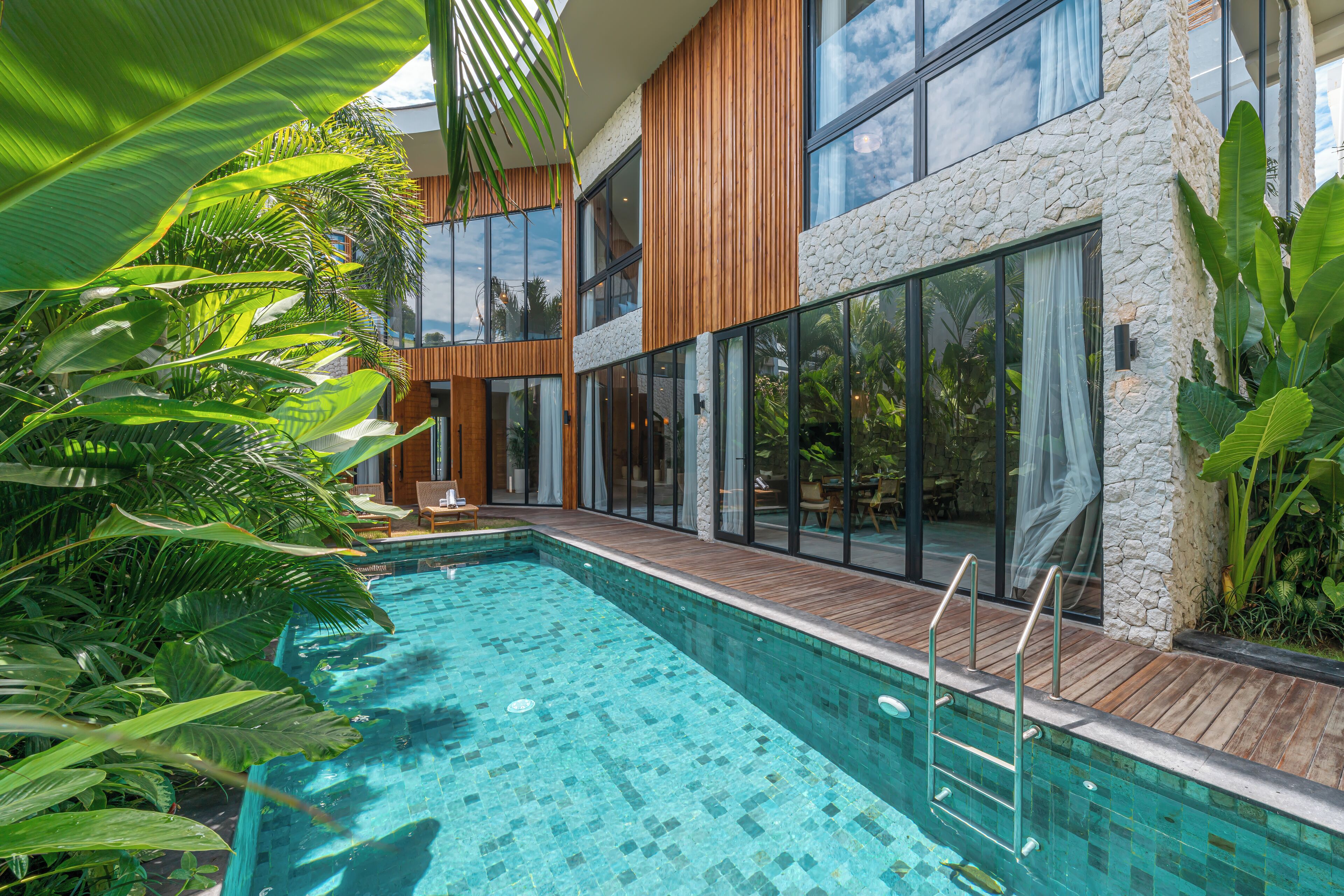 Uma área de piscina moderna com deck de madeira, paredes de pedra e grandes janelas.
