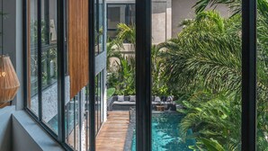 A modern building with large windows overlooking a swimming pool and lush greenery. - Villa Amanora (Canggu)