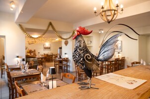 Un comedor con mesas y sillas de madera, una lámpara de araña y una estatua decorativa de gallo sobre una mesa.