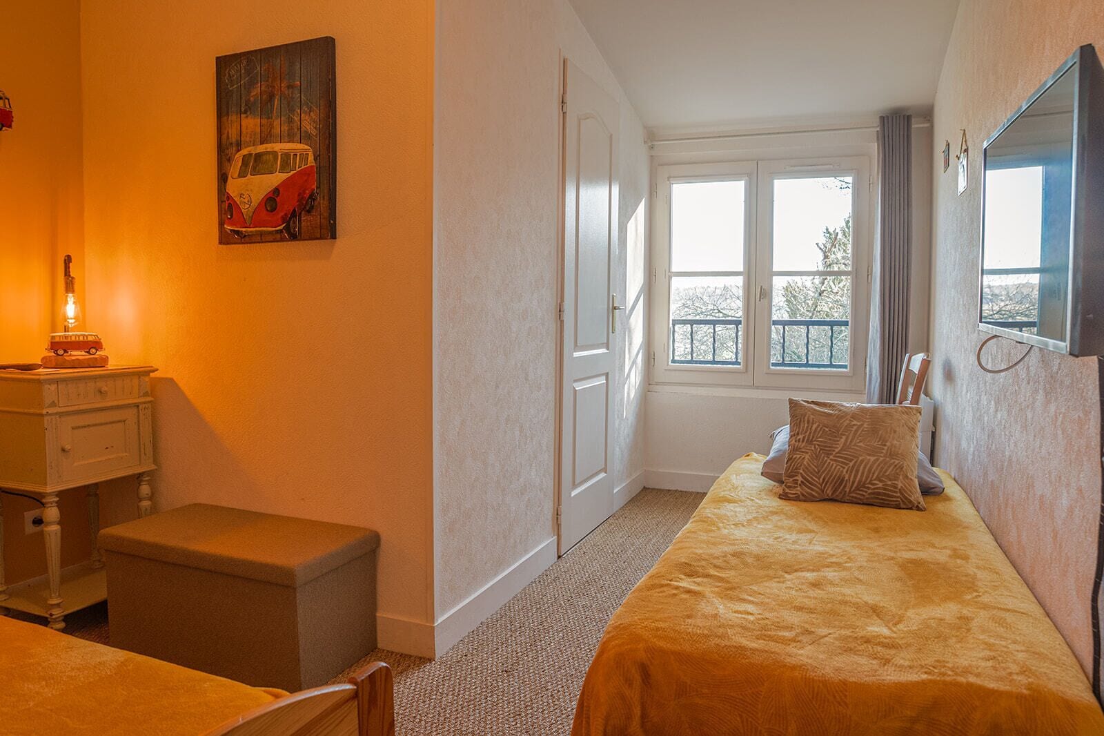 Un dormitorio con cama, mesita de noche, lámpara, ventana y un cuadro en la pared.
