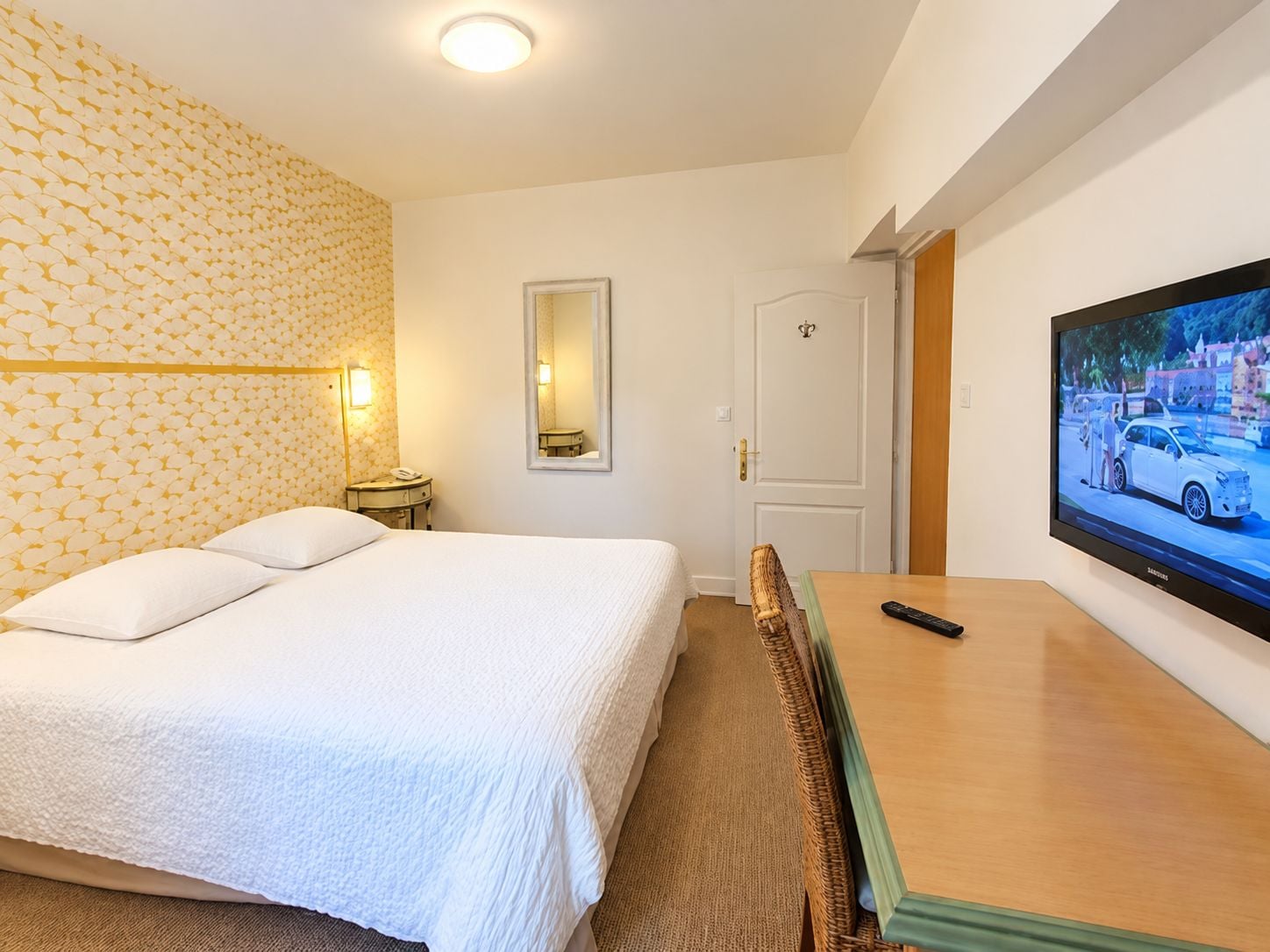 A hotel room with a bed, a television, a mirror, and a door.