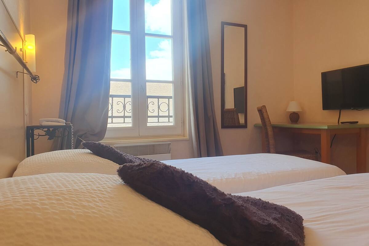 A hotel room with two beds, a desk with a chair, a television, and a window with curtains.