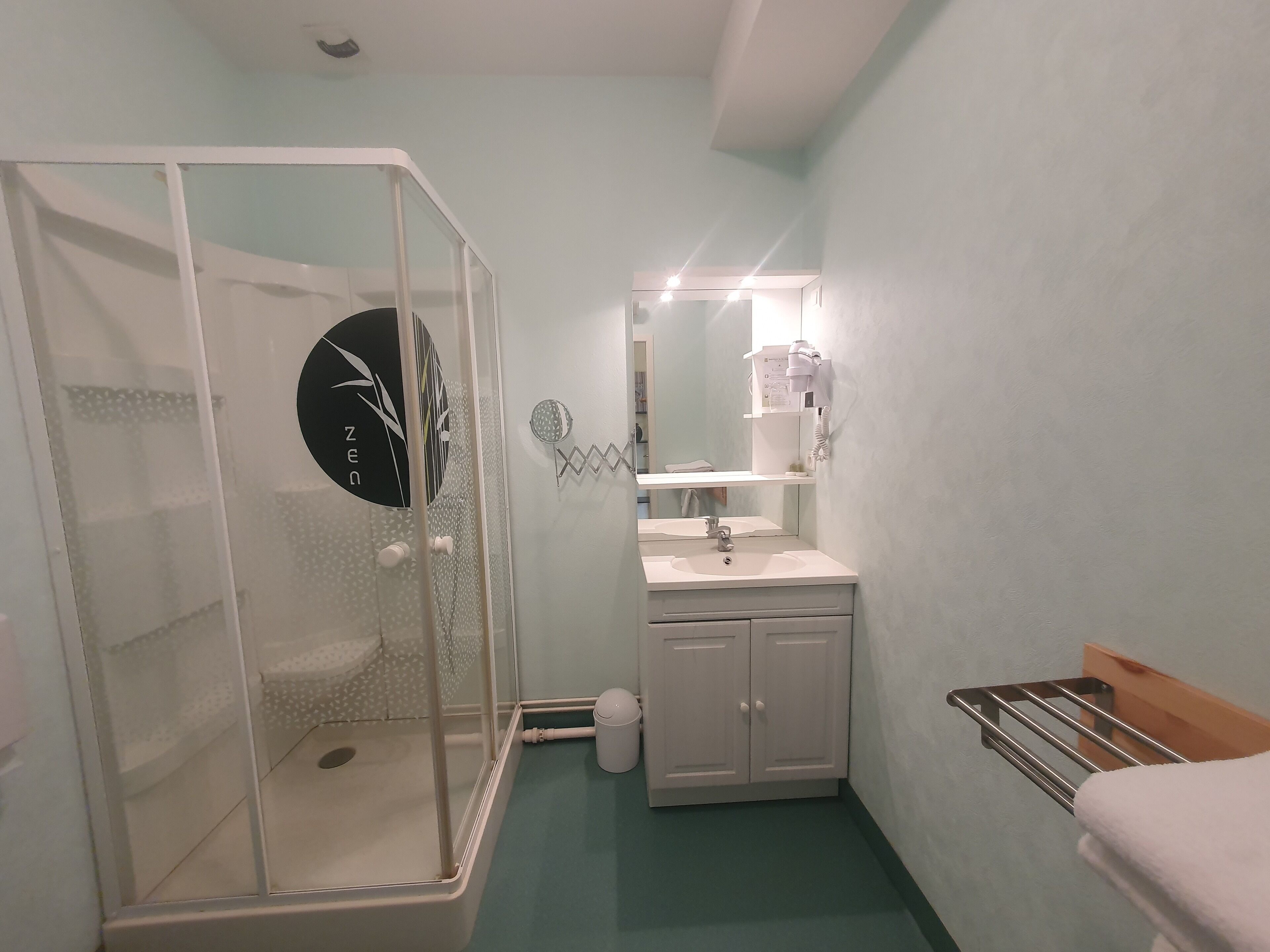 A bathroom with a glass shower enclosure, a sink with a mirror above it, and a towel rack.