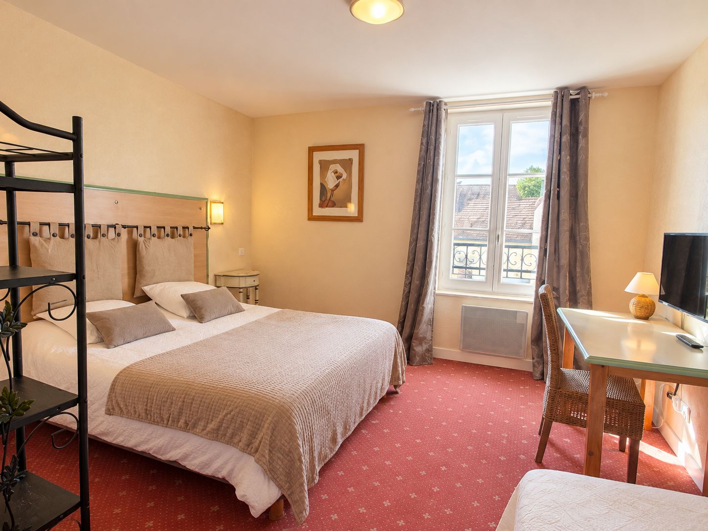 A hotel room with a bed, a desk with a chair, a television, and a window with curtains.