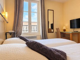 Una habitación de hotel con cama, escritorio con silla, televisor y ventana con cortinas.
