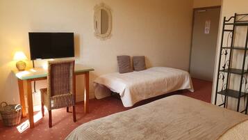 A room with two beds, a desk with a lamp, a television, a mirror, and a metal shelf unit.