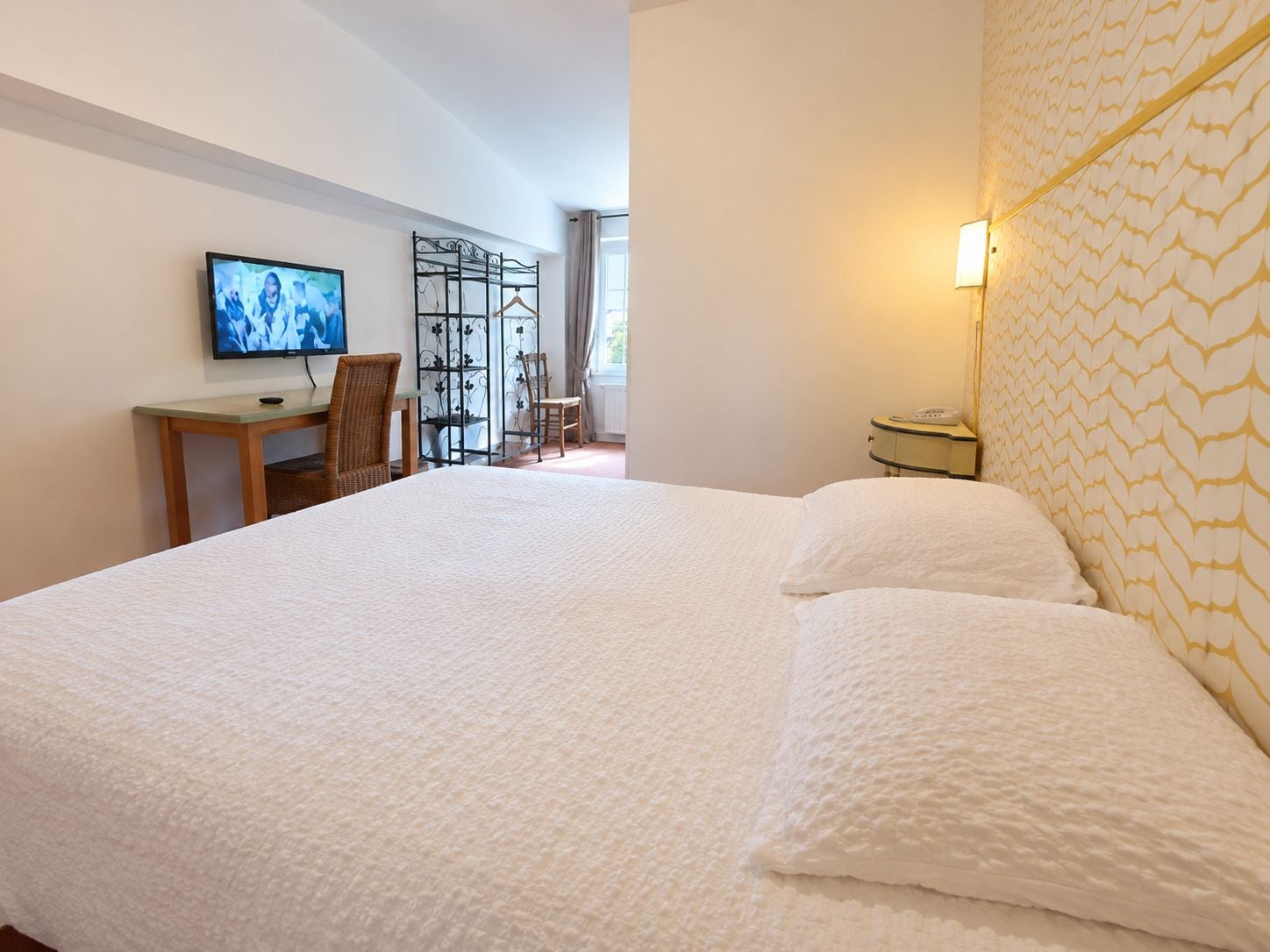 A hotel room with a large bed, a desk with a chair, a television, and a decorative screen.
