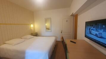 A hotel room with a bed, a bedside table, a mirror, a TV, and a door.