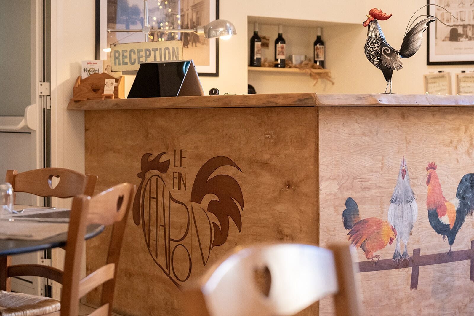 A wooden reception desk with a rooster logo and a painting of roosters on the wall.