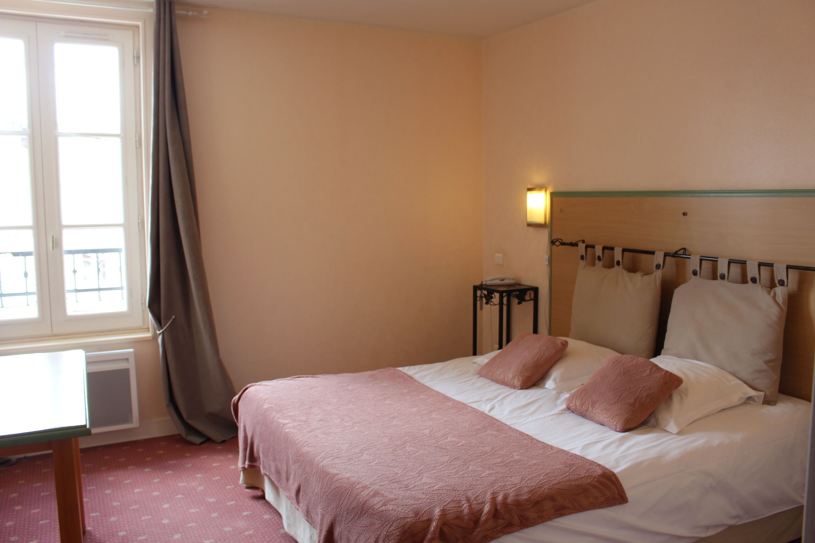 A hotel room with a bed, a bedside table, a lamp, and a window with curtains.