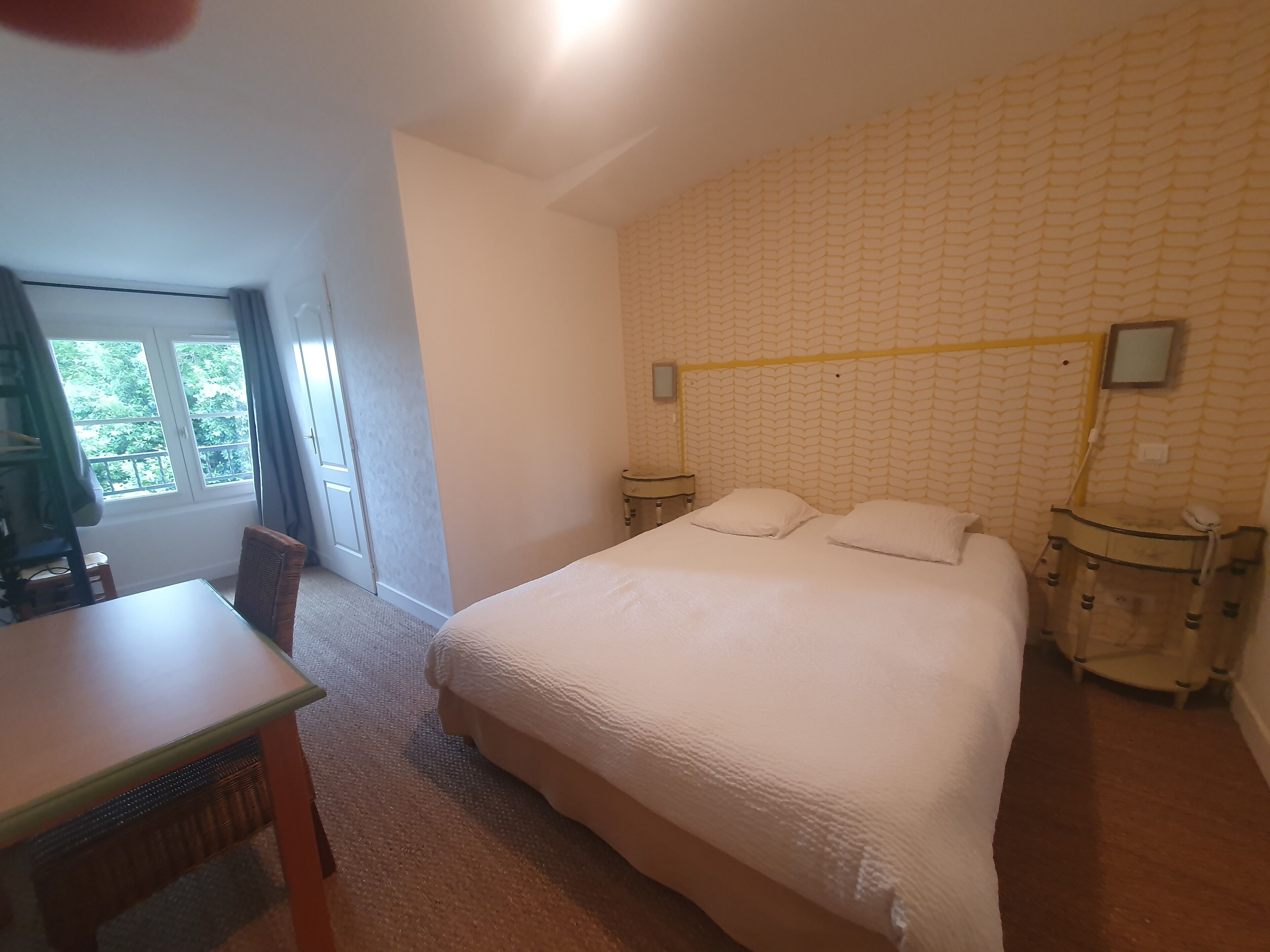 A bedroom with a bed, a desk, and a chair. There is a window with a view of trees.