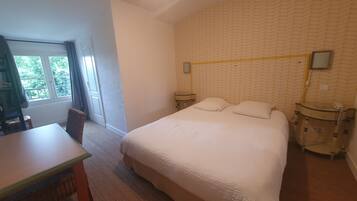 A bedroom with a bed, a desk, and a chair. There is a window with a view of trees.
