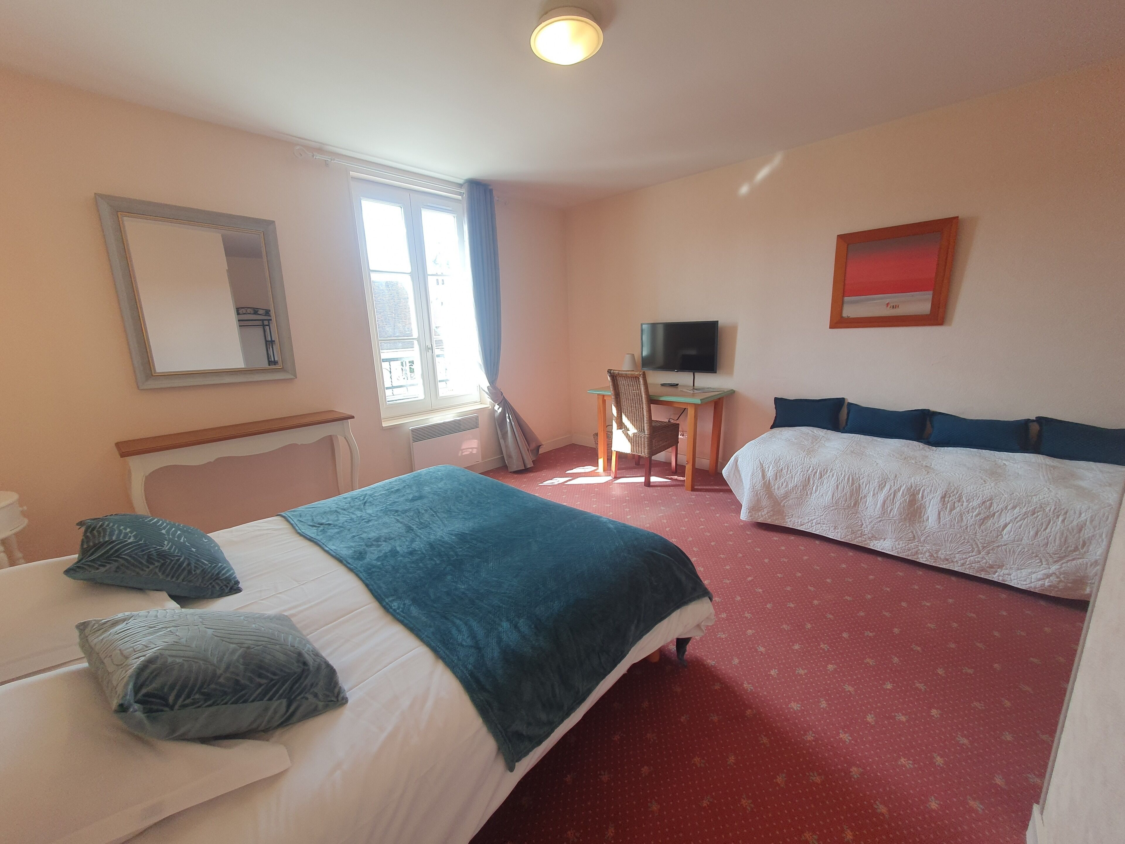 A hotel room with two beds, a desk with a television, a window with curtains, and a mirror on the wall.